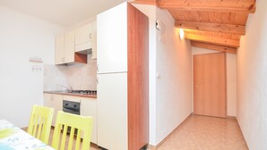 A compact kitchen with white cabinets, a wooden accent wall, a dining table with yellow chairs, and a tiled floor. - Apartment with old town view no.2 (Pirovac)