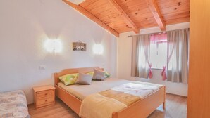 A bedroom with a wooden bed, bedside tables, a nightstand, a window with curtains, and a wall-mounted light fixture. - Apartment with old town view no.2 (Pirovac)
