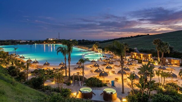 Un resort con una amplia piscina, tumbonas y una playa bien iluminada.