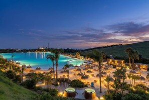 Een resort met een groot zwembad, ligbedden en een goed verlicht strand.