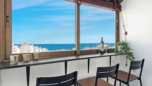 Ein Balkon mit Blick auf das Meer und Gebäude, mit einem Tisch, Stühlen, einer Kübelpflanze und Dekorationselementen.