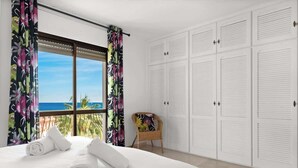 Ein Hotelzimmer mit Bett, Stuhl und Blick auf den Ozean.