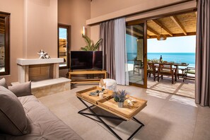 Un salon moderne avec un canapé, un téléviseur et une table basse en bois. Il y a un balcon avec vue sur la mer.