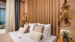 Habitación de hotel con cama, ropa de cama blanca, cabecera de madera, mesita de noche con una planta y vistas al exterior.