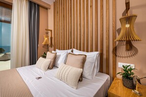A hotel room with a bed, white bedding, a wooden headboard, a side table with a plant, and a view of the outdoors.