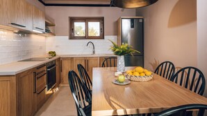 A modern kitchen with wooden cabinets, a stainless steel refrigerator, a dining table with chairs, and a vase with lemons. - Terra Lucis Mountain Residences Mare Villa (Zakynthos)