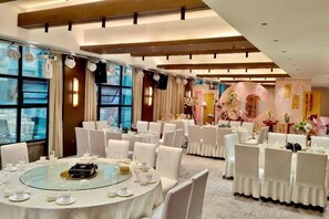 A banquet hall with round tables set for dining, large windows, and a decorative wall with floral arrangements. - Jiuzhou Jindu Hotel (Pingwu)