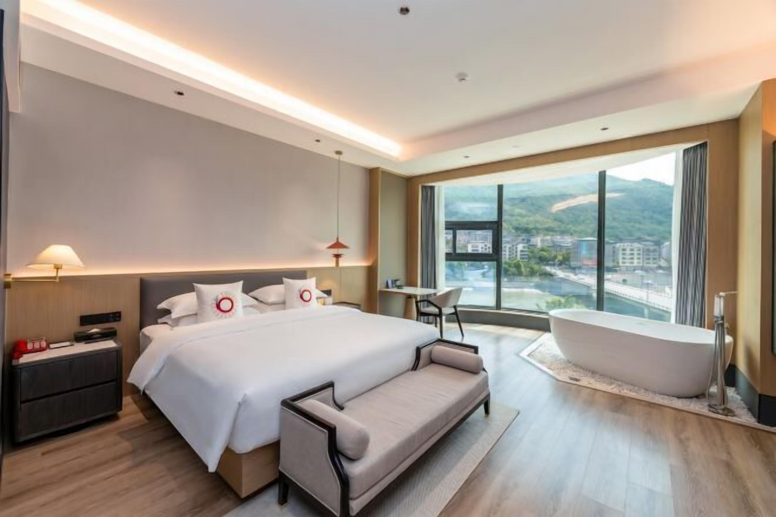 Une chambre d’hôtel moderne dotée d’un grand lit, d’un coin salon, d’une baignoire et offrant une vue sur la ville.