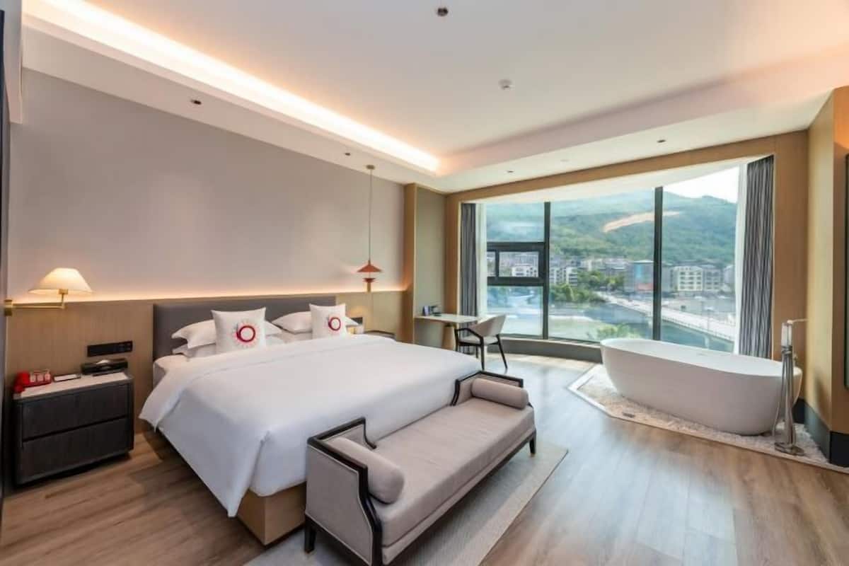 Une chambre d’hôtel moderne dotée d’un grand lit, d’un coin salon, d’une baignoire et offrant une vue sur la ville.