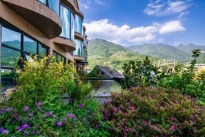 Un edificio moderno con amplios ventanales, una fuente de agua y abundante vegetación.