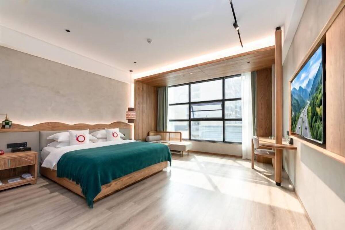 Une chambre d’hôtel moderne avec un grand lit, un bureau, une chaise et une grande fenêtre.