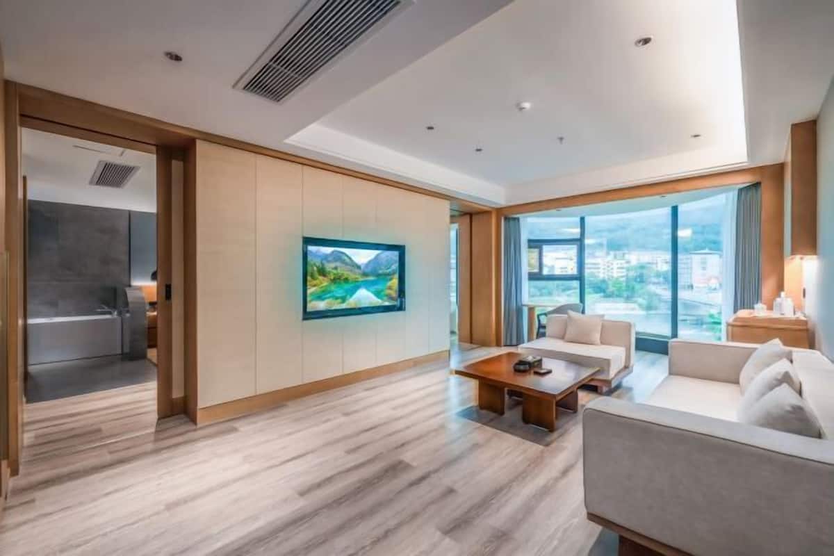 Une chambre d’hôtel moderne avec un plancher en bois, une grande fenêtre, un canapé, une table basse et un tableau au mur.