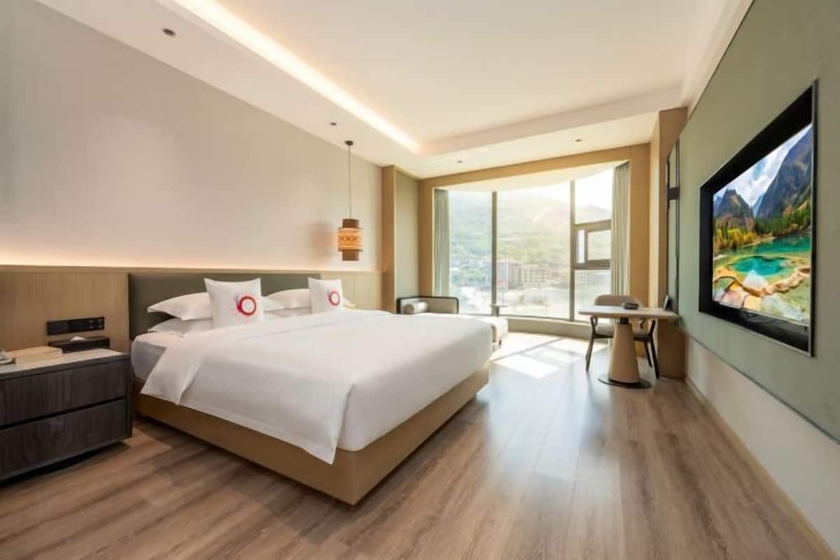 Une chambre d’hôtel moderne avec un grand lit, des tables de chevet, un bureau et une grande fenêtre.