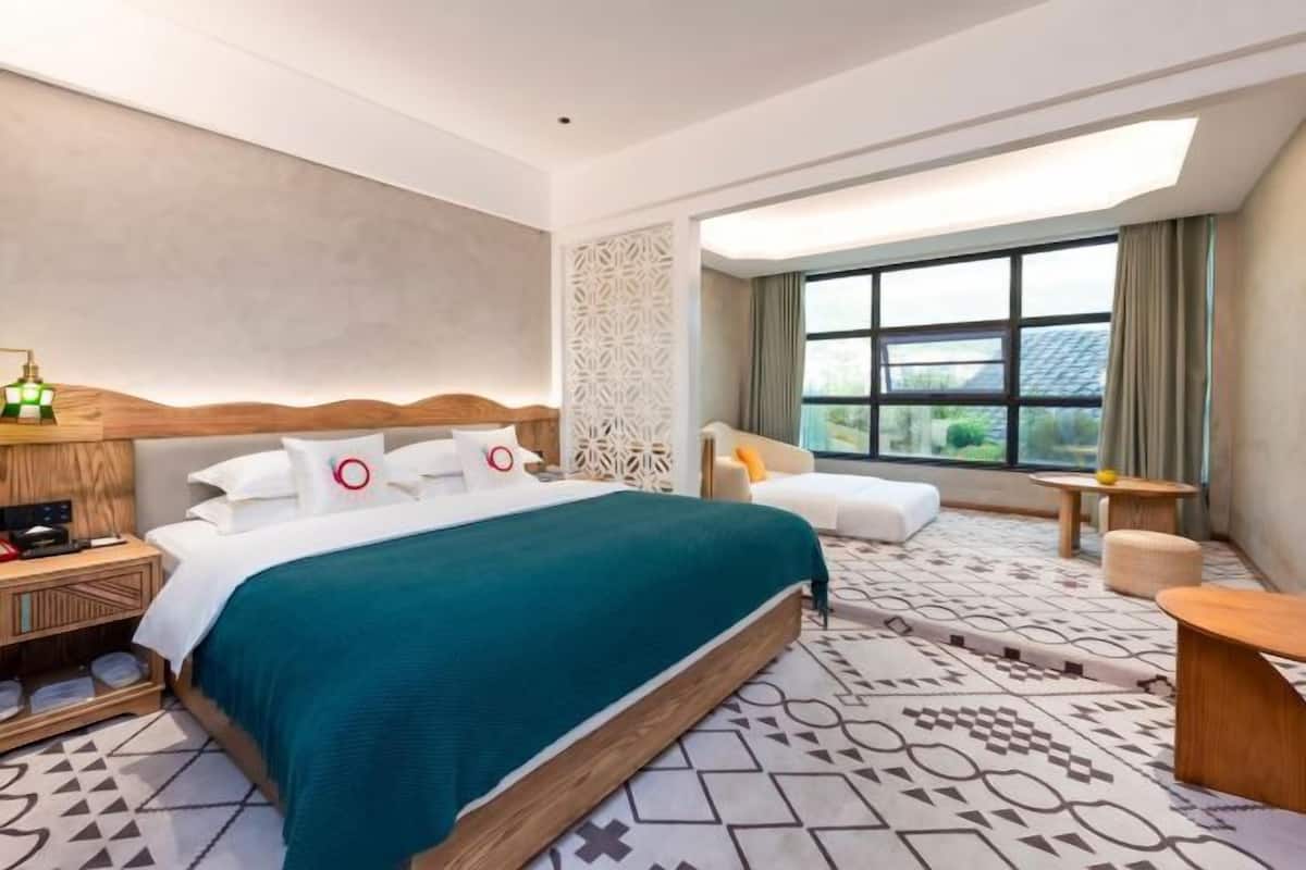 Une chambre d’hôtel avec un grand lit, un bureau, une chaise et une fenêtre donnant sur un beau paysage.