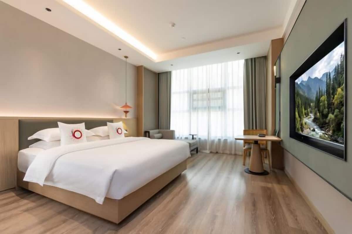 Une chambre d’hôtel moderne dotée d’un grand lit, d’un bureau, d’une chaise et d’une grande fenêtre offrant une vue sur les montagnes.