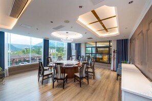 A modern hotel room with a large dining table, comfortable seating, and a view of the mountains. - Jiuzhou Jindu Hotel (Pingwu)