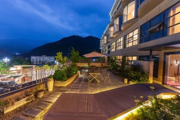 A hotel courtyard with outdoor seating, a wooden deck, and a mountain view in the background. - Jiuzhou Jindu Hotel (Pingwu)