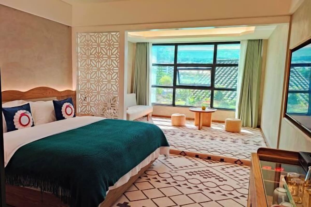 Een hotelkamer met een groot bed, uitzicht op de omgeving, een klein tafeltje en een decoratief wandpaneel.