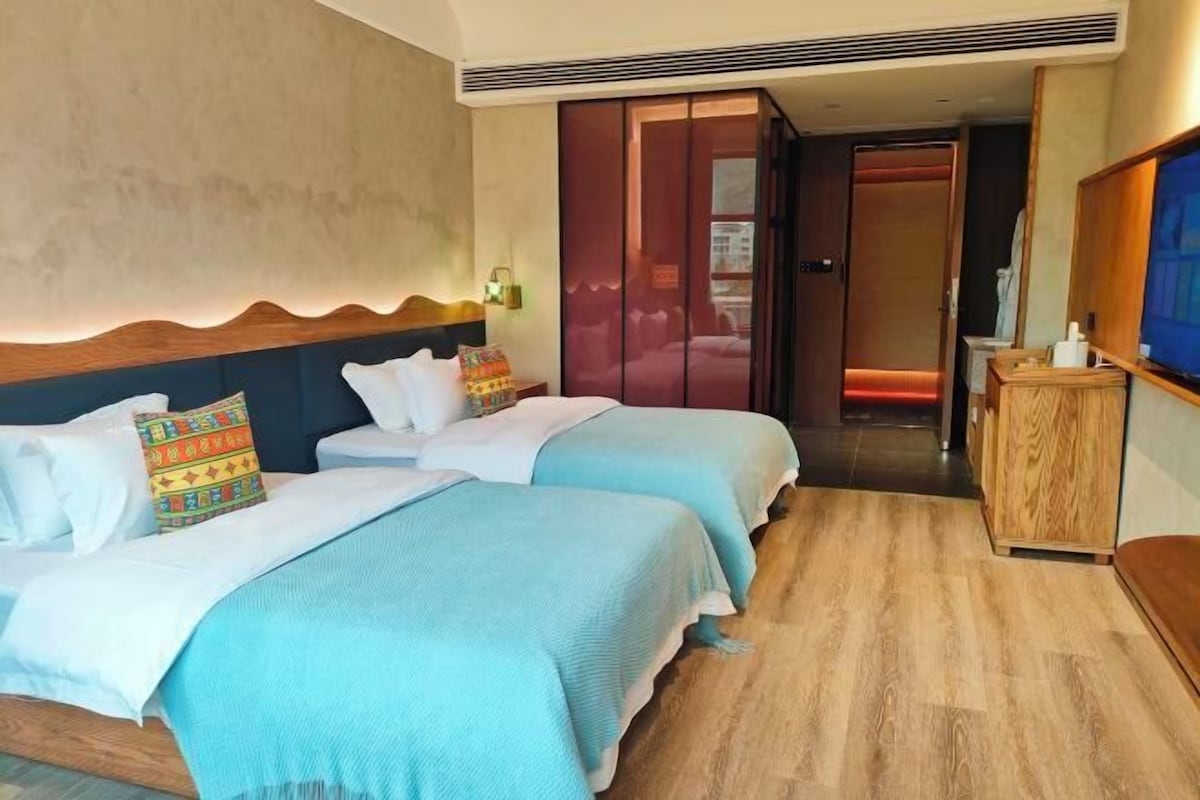 Een hotelkamer met twee bedden, een houten vloer, een televisie en een kledingkast.
