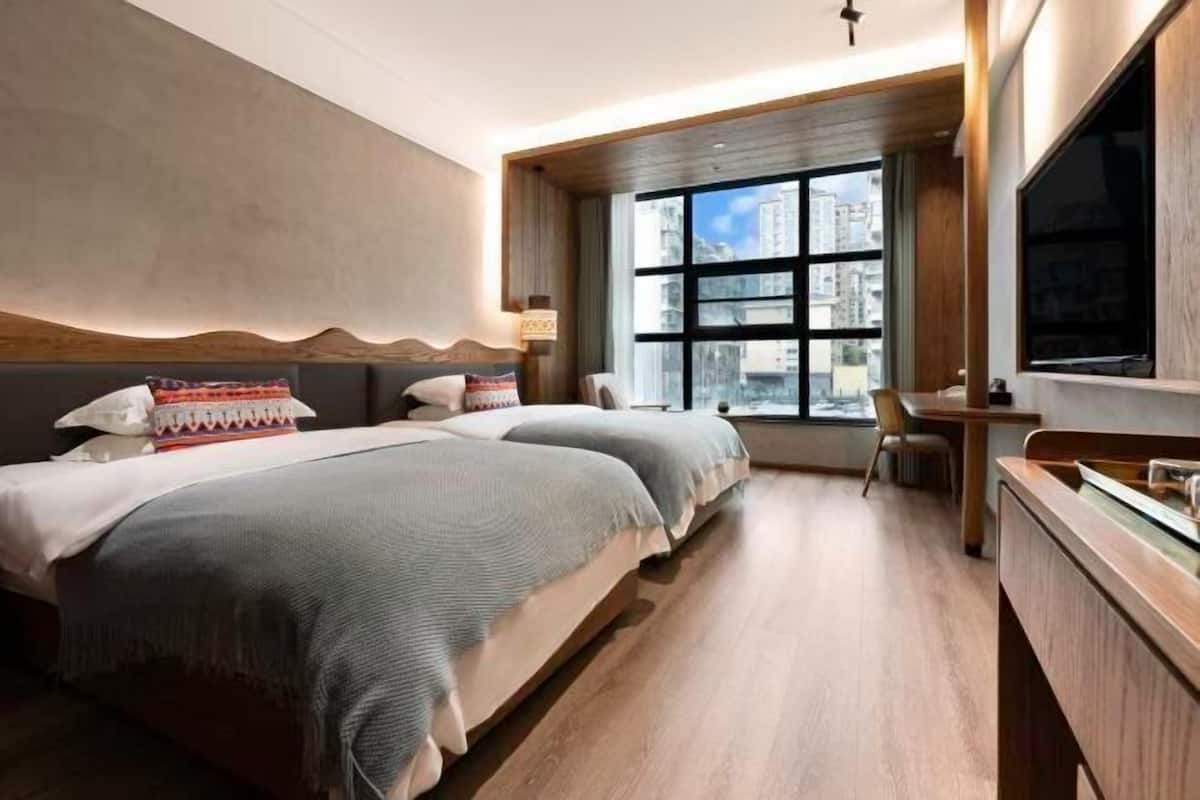 Une chambre d’hôtel moderne, dotée de deux lits, d’un bureau, d’une télévision et d’une grande fenêtre donnant sur la ville.
