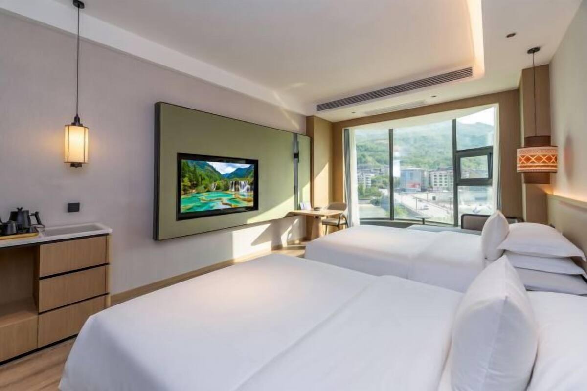 Une chambre d’hôtel avec deux lits, une télévision, un bureau et une grande fenêtre donnant sur un beau paysage.