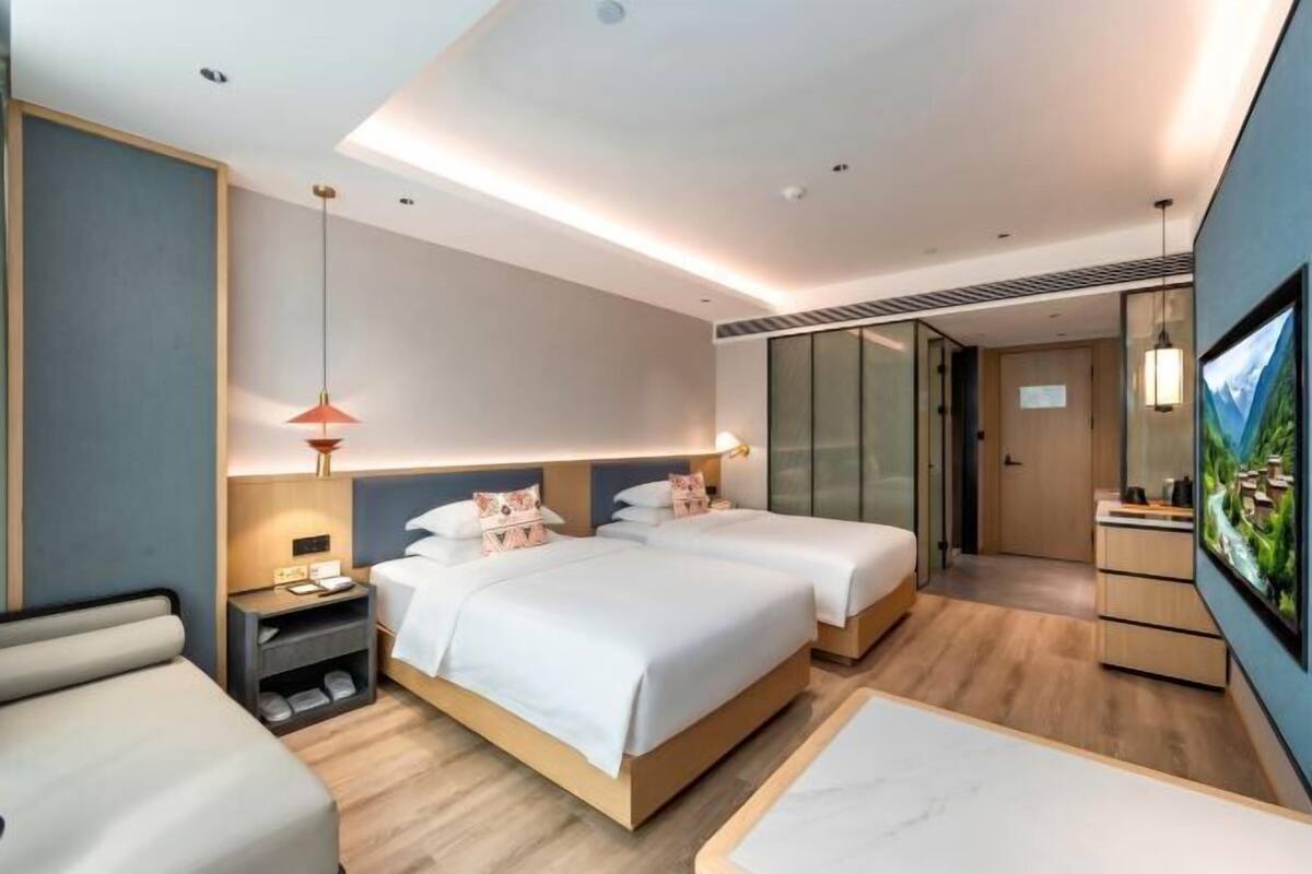 Une chambre d’hôtel moderne équipée de deux lits, d’un bureau, d’une télévision et d’une porte coulissante donnant accès à la salle de bain.