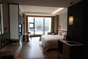 Een moderne hotelkamer met een groot bed, een bureau, een stoel, een kleine tafel, een televisie en een groot raam met uitzicht op de stad.