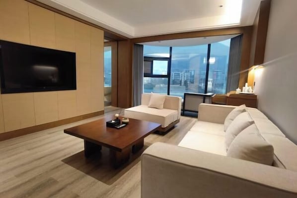 Een moderne hotelkamer met een groot raam met uitzicht over de stad, een flatscreen televisie aan de muur en een comfortabele zithoek met een bank en een salontafel.