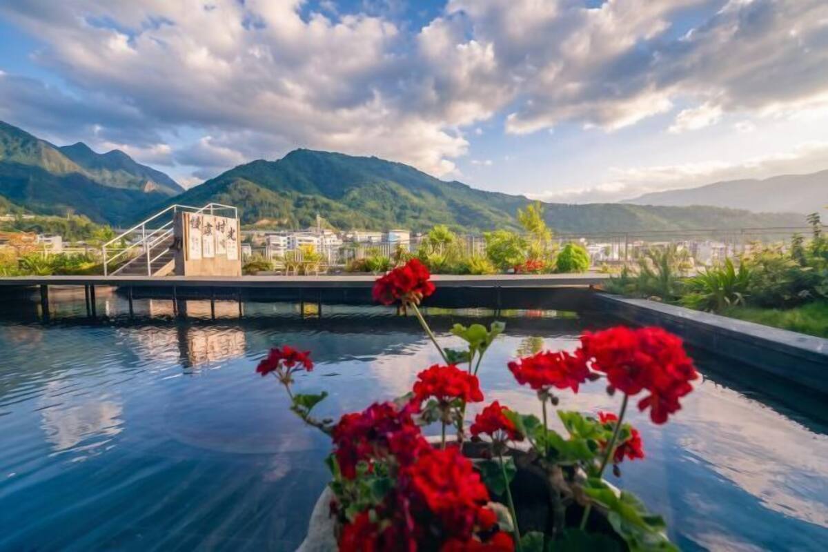 Une piscine avec une chaîne de montagnes en arrière-plan, un pont et des fleurs rouges au premier plan.