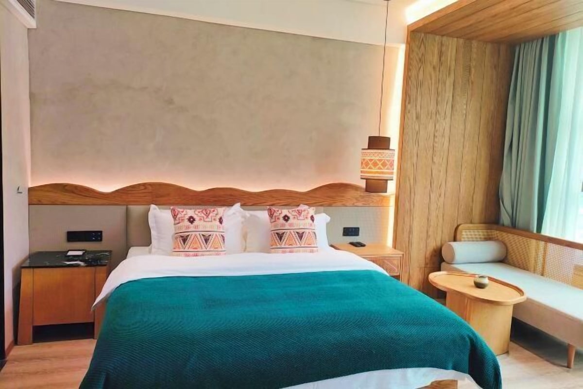 Hotelkamer met een groot bed, nachtkastje, stoel en raam met gordijnen.