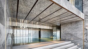 A modern interior with a glass staircase leading to a lower level, surrounded by marble walls and a reflective floor. - Lovely 3BR Apt with Panoramic Views, FREE Parking (Melbourne)