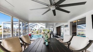 A covered patio with a pool, outdoor seating, and a ceiling fan. - VRCC Villa Golden Retreat (Cape Coral)