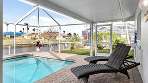 A covered outdoor swimming pool area with lounge chairs, a view of a residential neighborhood, and a clear sky. - VRCC Villa Golden Retreat (Cape Coral)
