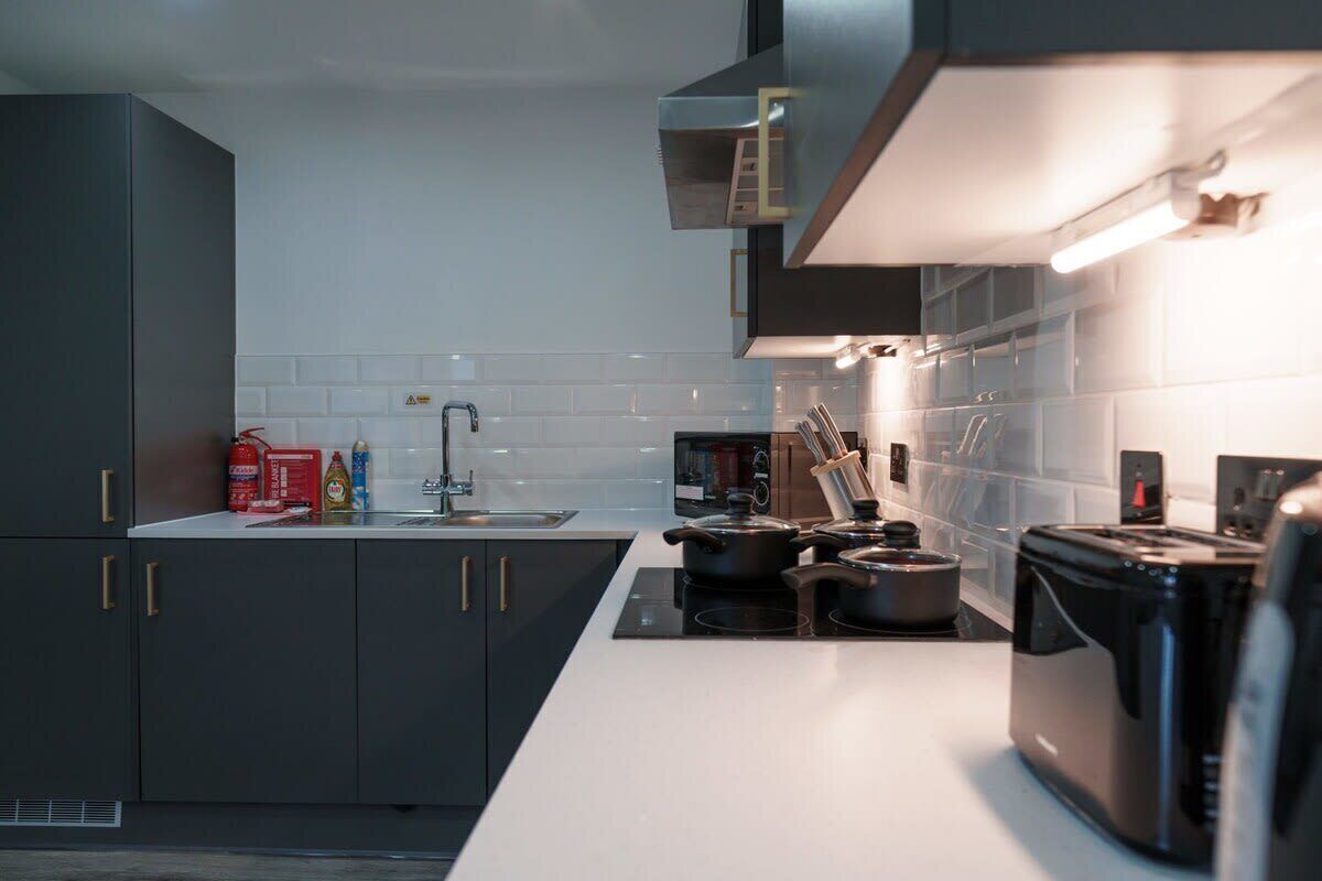 Une cuisine moderne avec des meubles de couleur sombre, un plan de travail blanc, une cuisinière et un grille-pain.