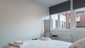 A hotel room with a large bed, a window with a view of buildings, a radiator, and a mirror on the wall. - Spacious 1BED Flat in Central Preston fast WiFi (Preston)