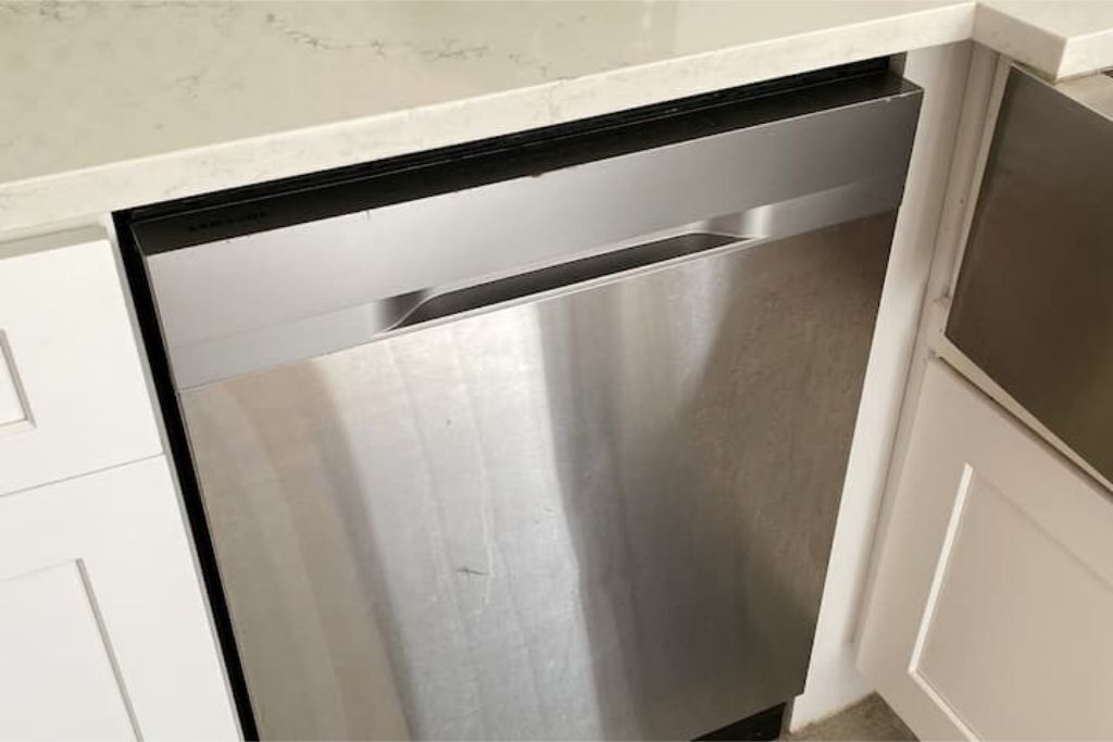 Un lave-vaisselle en acier inoxydable dans une cuisine avec des armoires blanches et un plan de travail blanc.