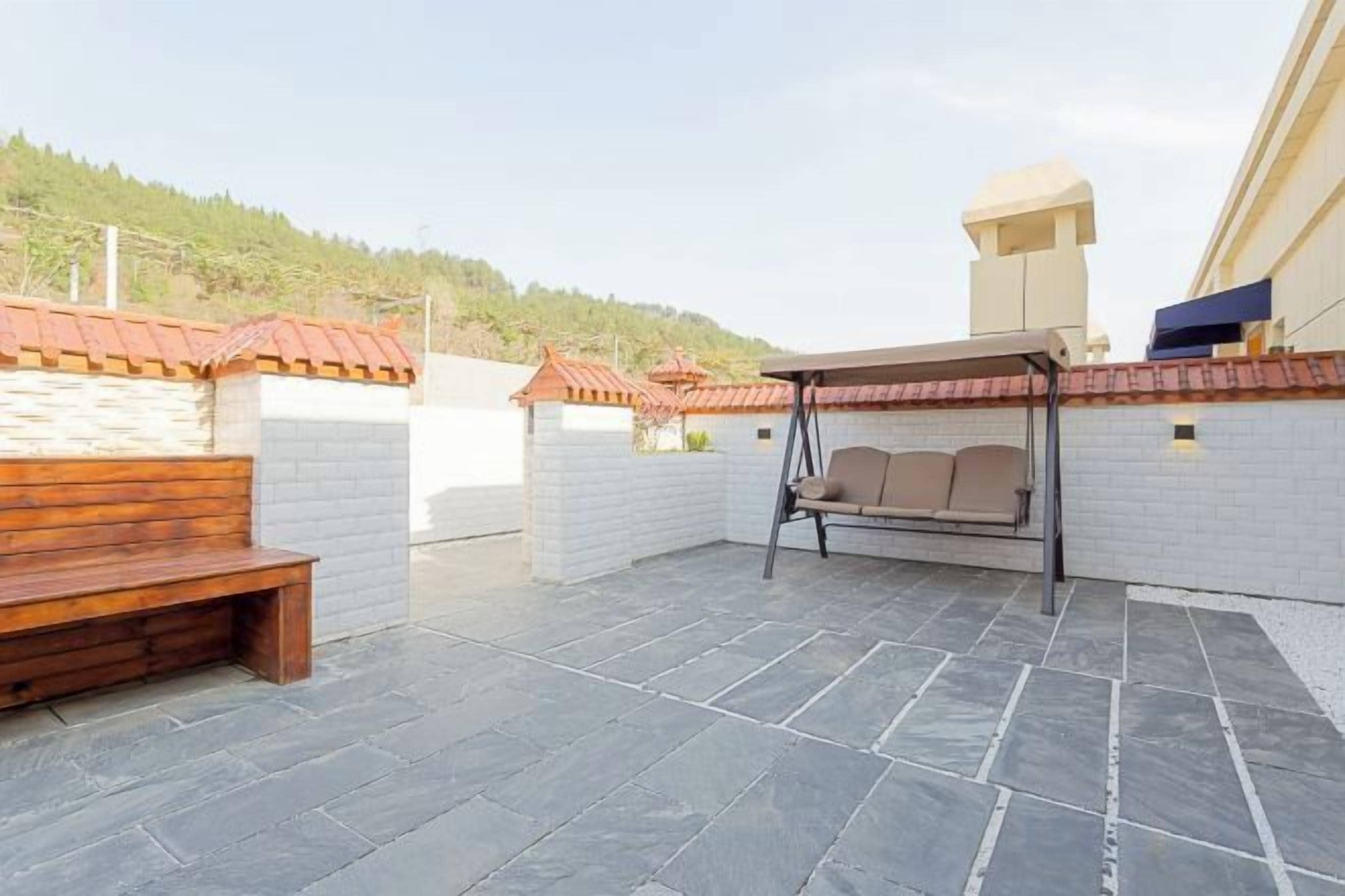 A rooftop patio with a swing, a bench, and a view of a hill.