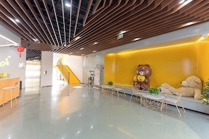 Un vestíbulo moderno con techo de madera, una recepción, una pared amarilla con decoración de oso y una escalera al fondo.