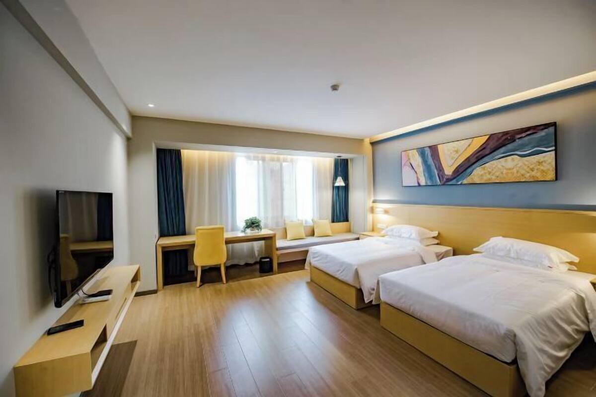 A hotel room with two beds, a desk, a TV, and a painting on the wall.