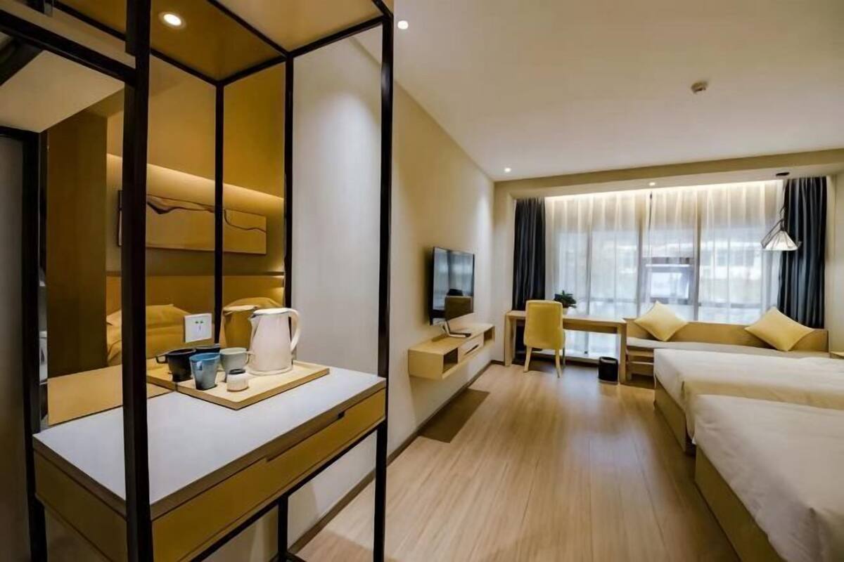 A hotel room with a bed, a desk, a chair, a TV, and a window with curtains.