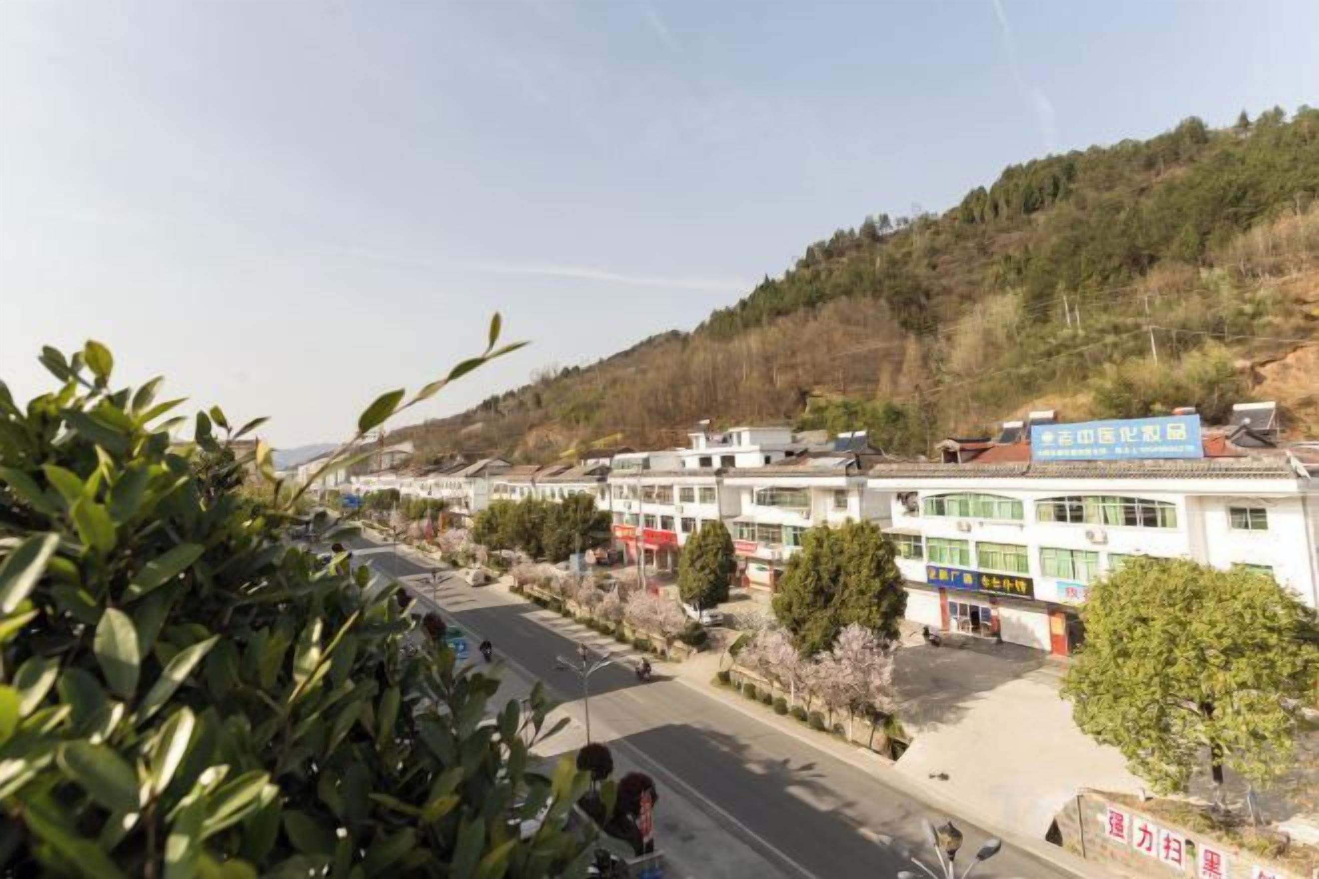 A street view with buildings, a clear sky, and a hilly landscape.