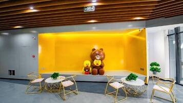 Un vestíbulo con una pared amarilla, un oso de peluche grande y dos osos más pequeños. Hay cuatro sillas y una mesa.