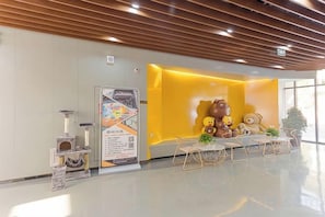 A reception area with a yellow wall, a large teddy bear decoration, and a seating area with tables and chairs. - Mini Home Boutique Hotel (Shiquan)
