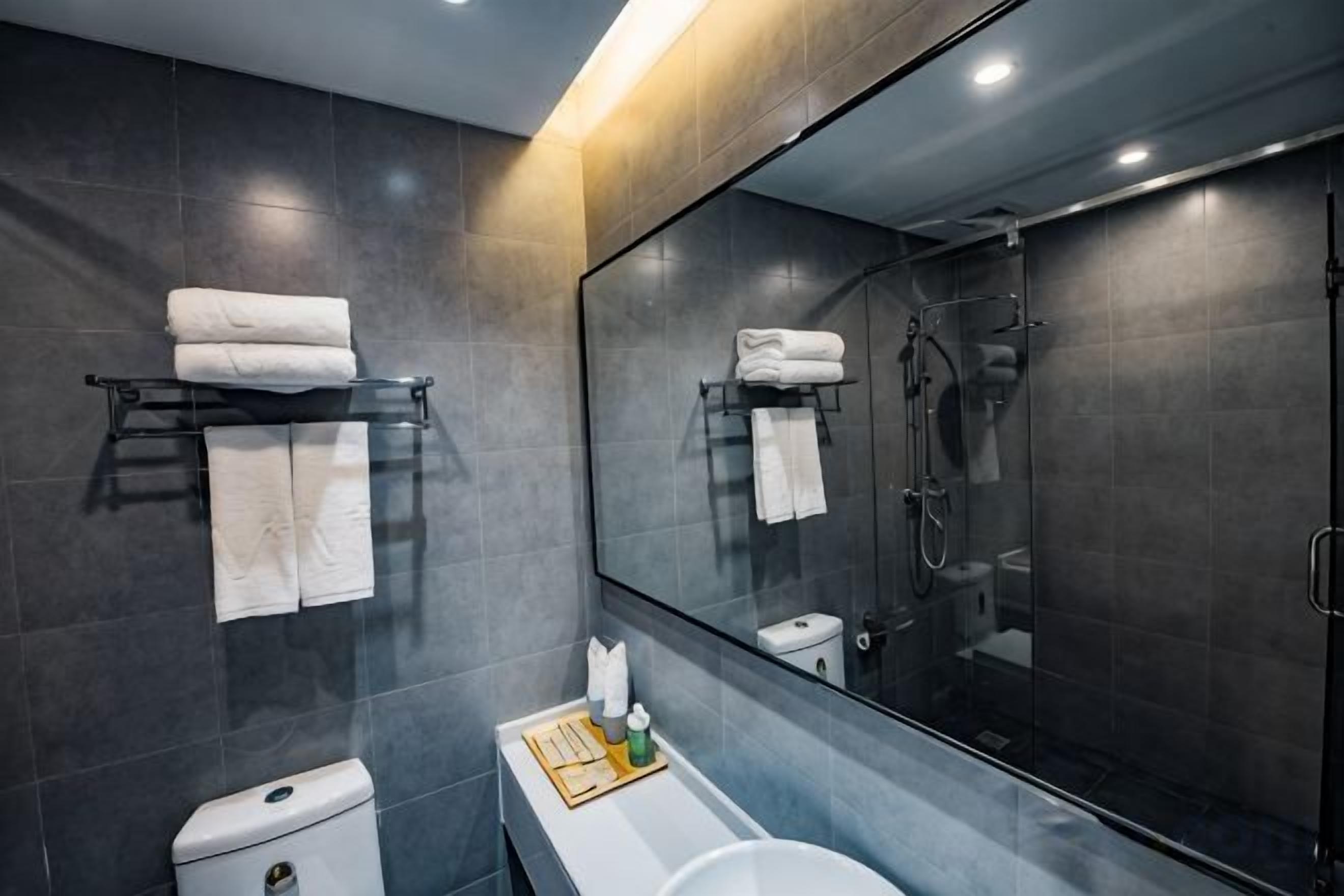 A modern bathroom with a toilet, sink, and shower. There are towels on a rack and a mirror above the sink.