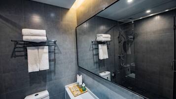 A modern bathroom with a toilet, sink, and shower. There are towels on a rack and a mirror above the sink.