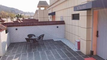 A rooftop patio with a table and chairs, a small trash bin, and a building entrance.