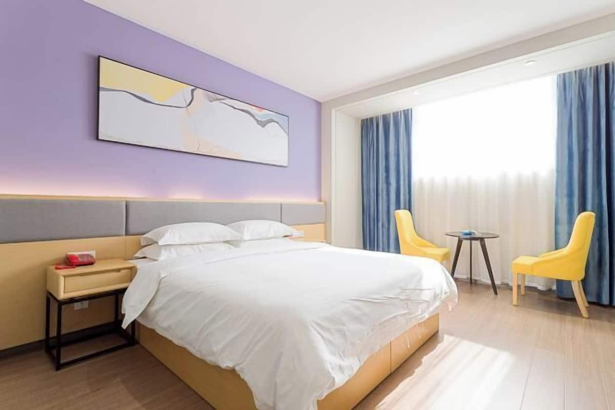 A hotel room with a bed, a bedside table, a chair, a small table, and a window with curtains.