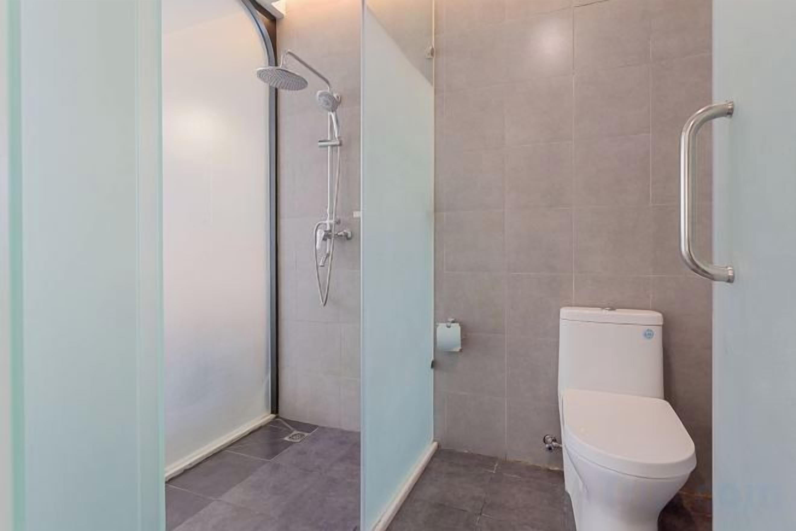A modern bathroom with a glass shower enclosure, a white toilet, and a handrail on the wall.