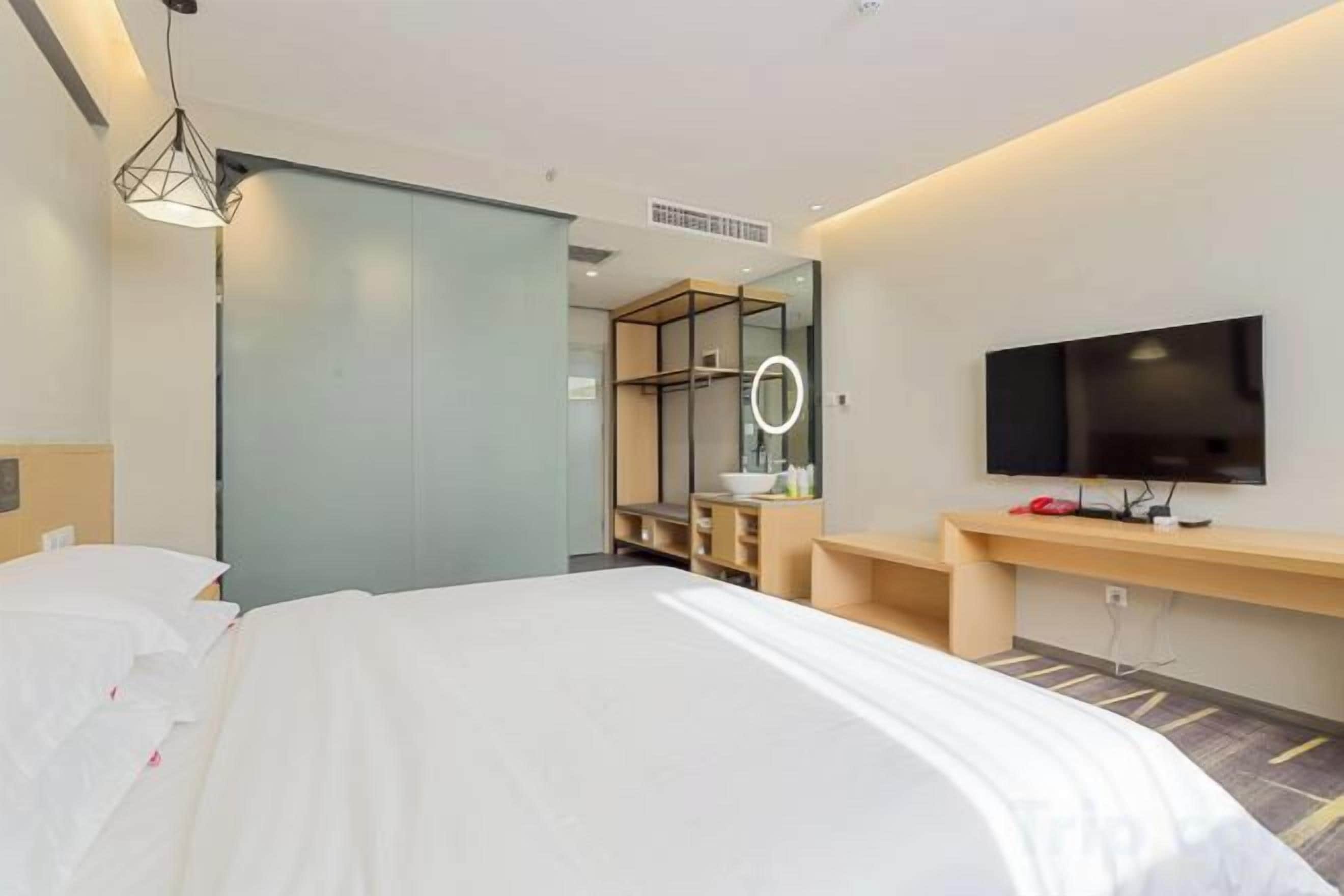A hotel room with a bed, a TV, a mirror, and a desk with a lamp.
