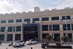 A modern building with a large entrance, several windows, and a parking lot with cars and a motorcycle. - Mini Home Boutique Hotel (Shiquan)